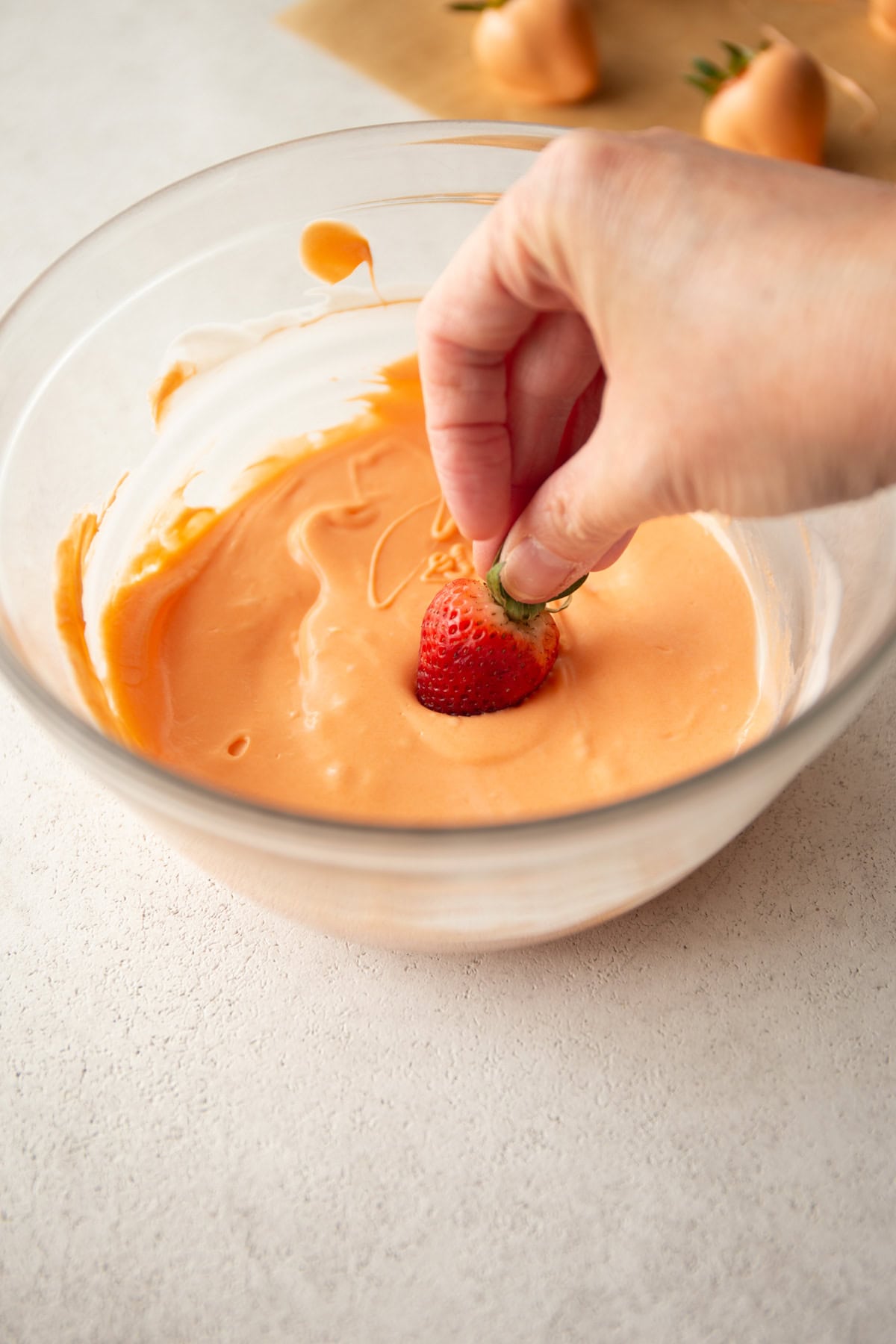 dipping a whole strawberry into orange tinted chocolate