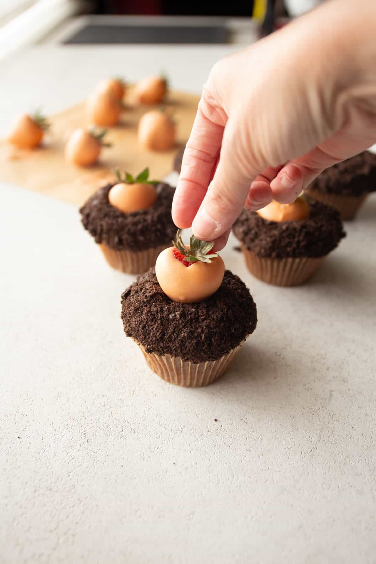 adding chocolate dipped strawberry to the top of a cupcake
