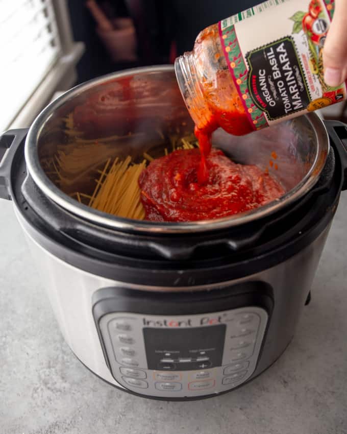 pouring marinara sauce over spaghetti in an instant pot
