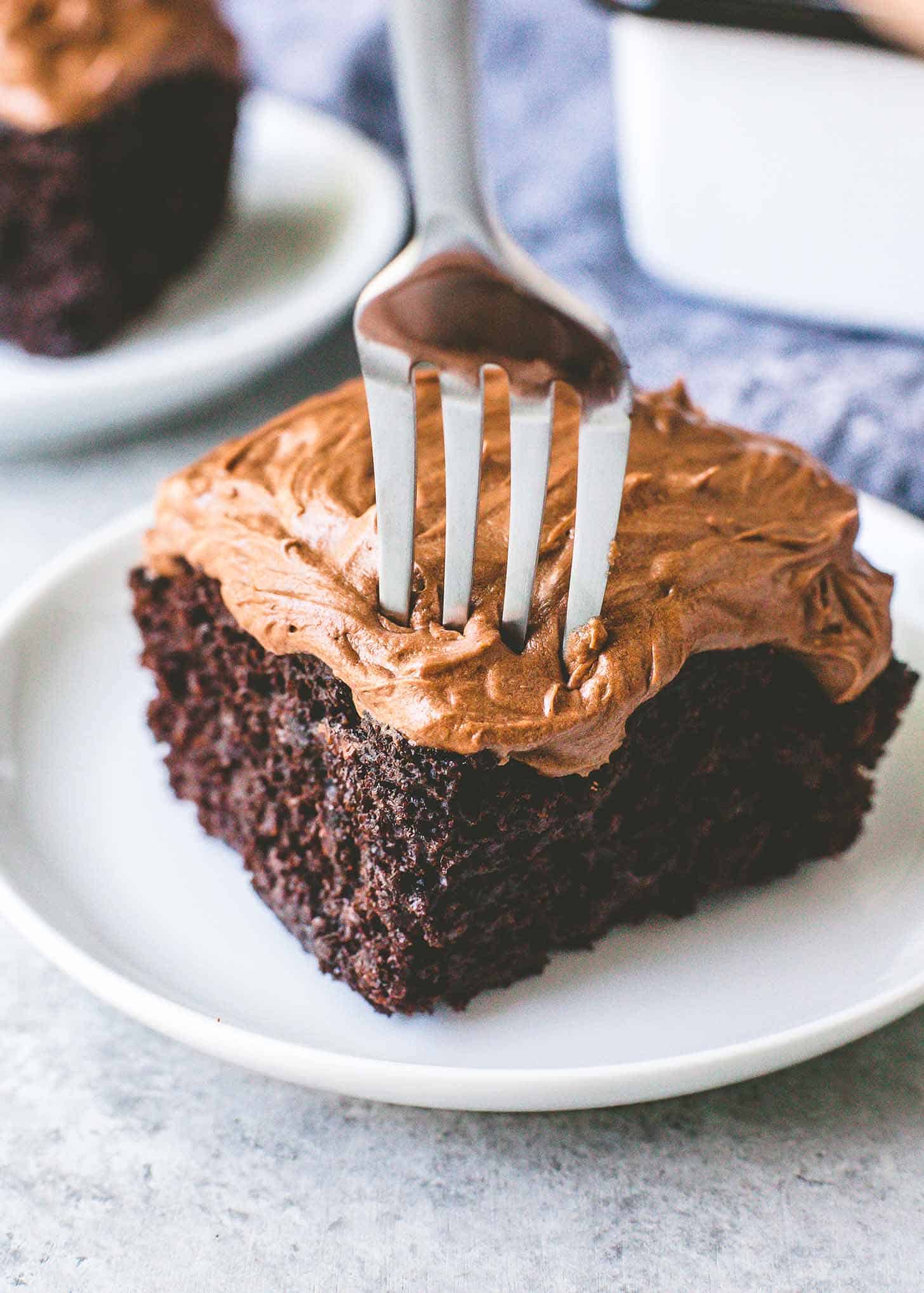 close up image of a fork in a piece of chocolate cake on a white plate