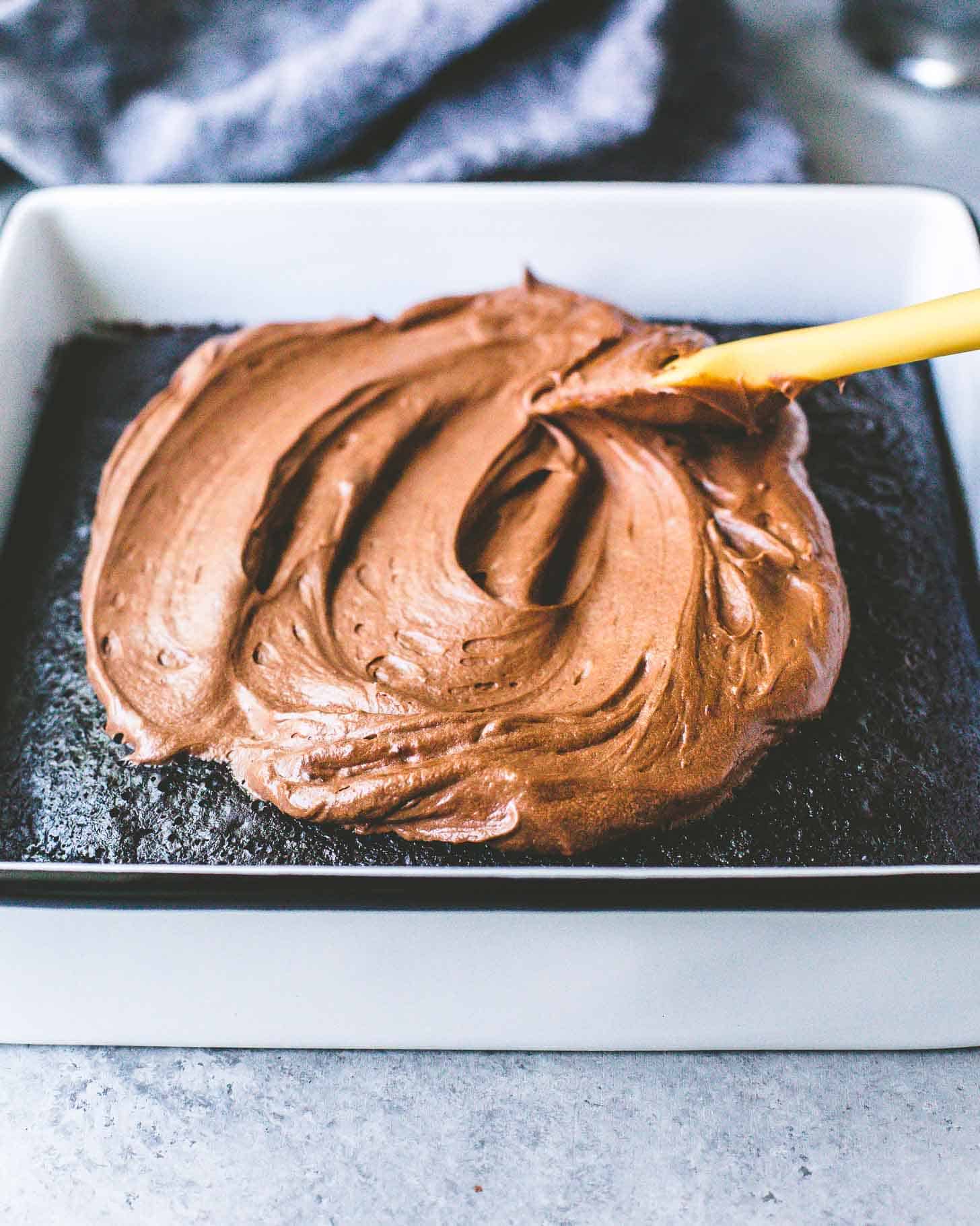 frosting a chocolate cake in a square baking dish