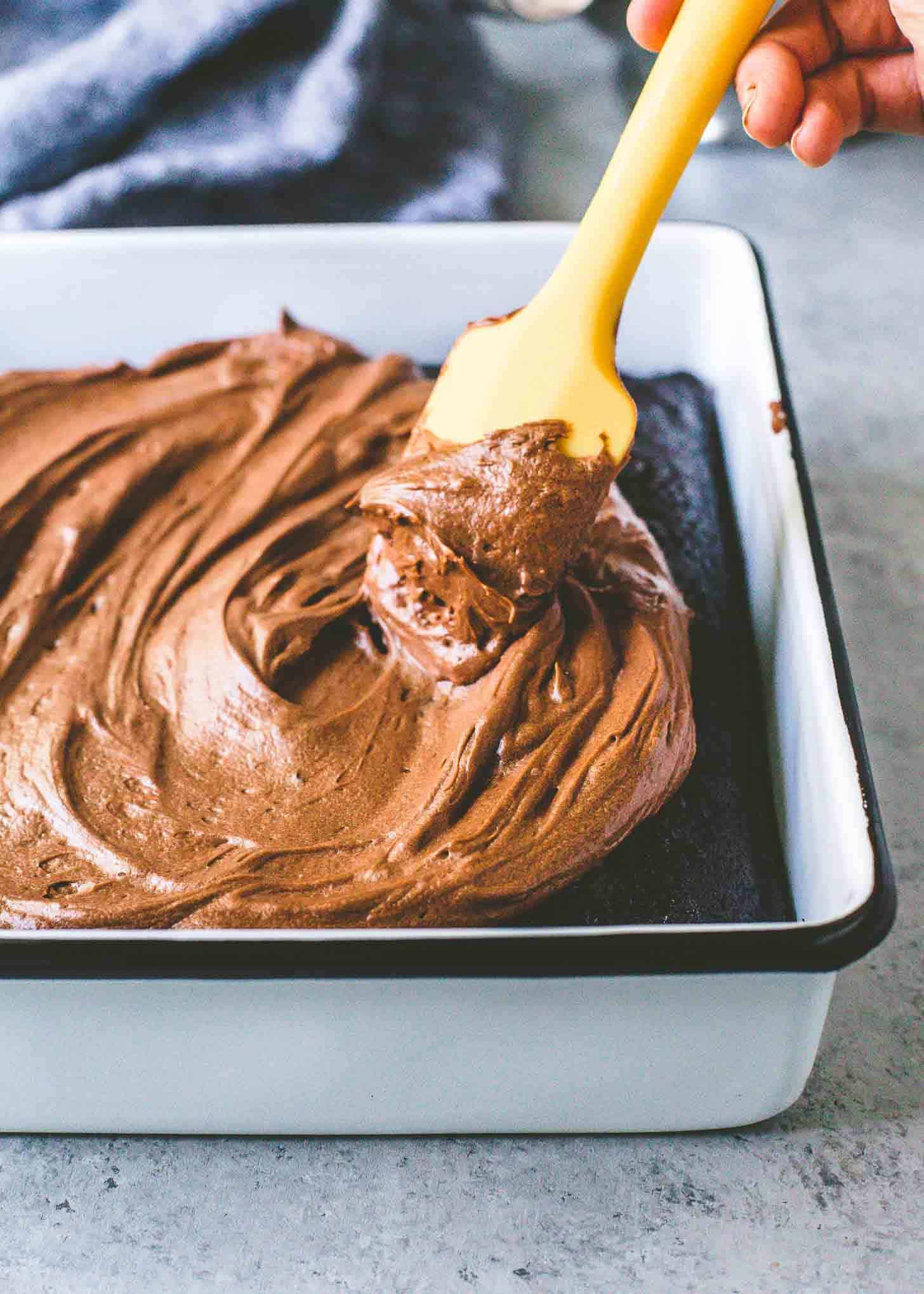 icing a chocolate cake in a square baking dish