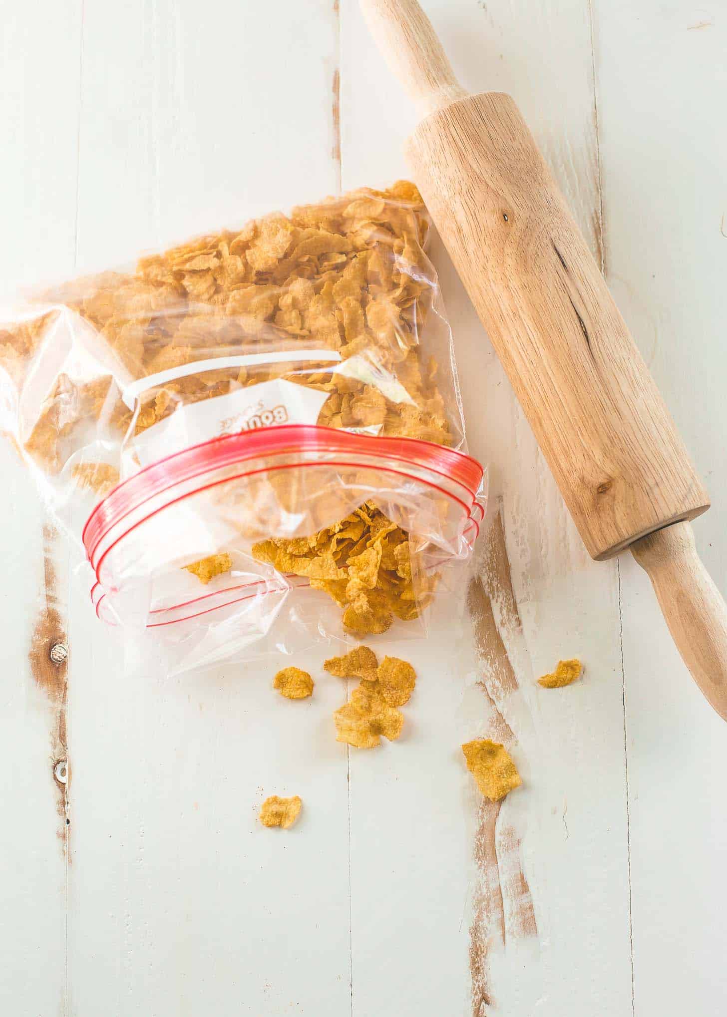 a freezer bag of cornflakes and a rolling pin on a white table