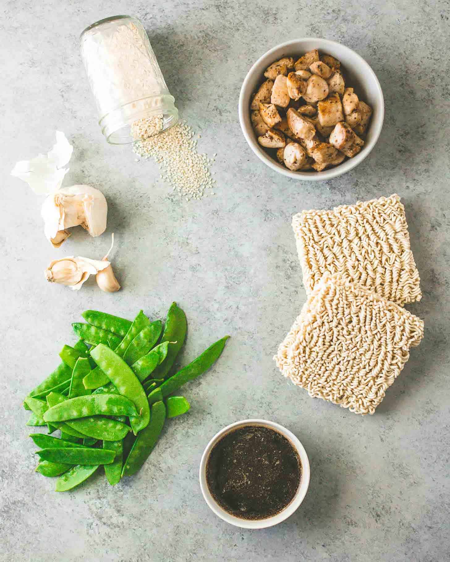 overhead image of Snow peas, sauce, ramen noodles, chicken and spices on a grey counter