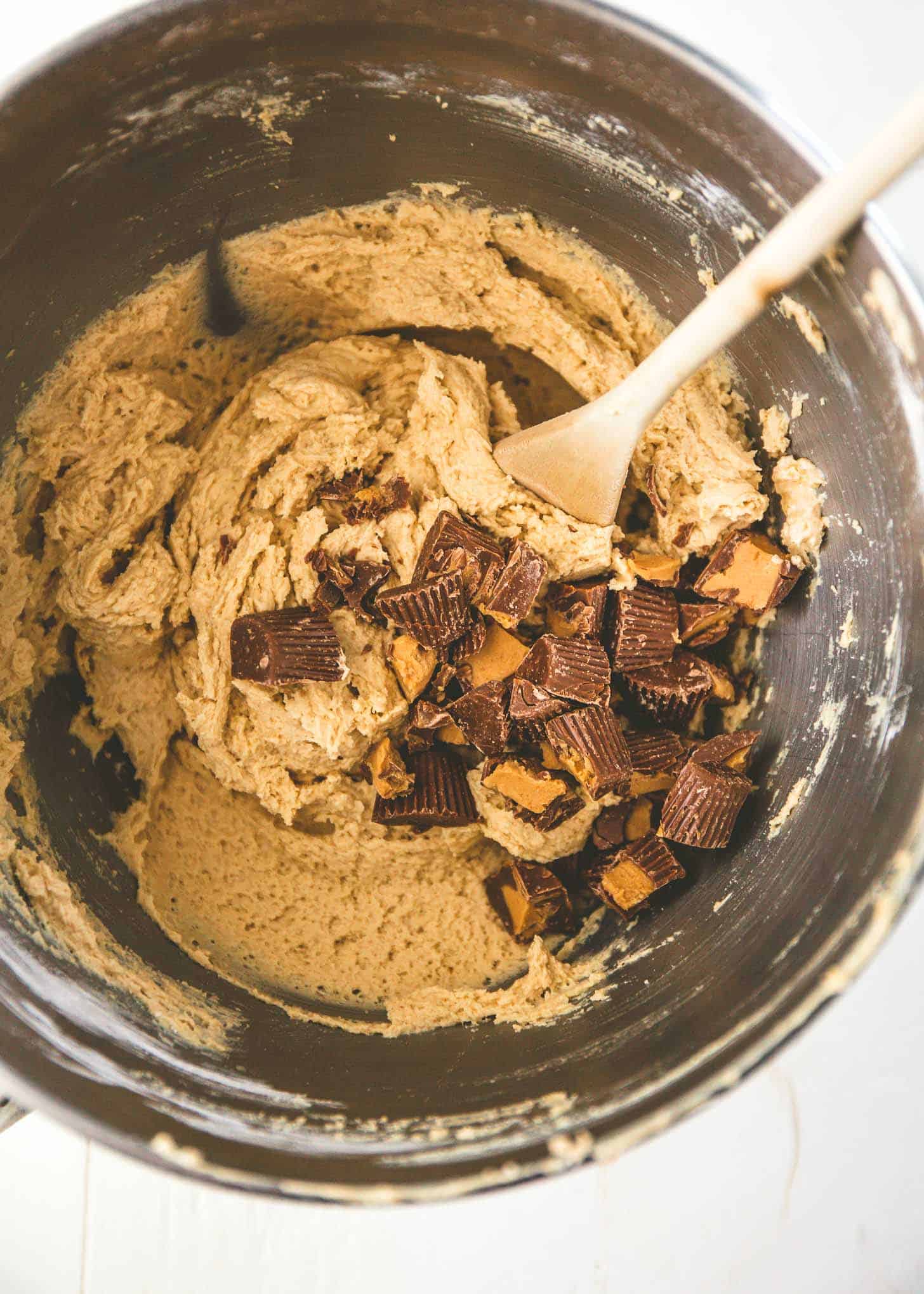 overhead image of a wooden spoon mixing peanut butter cups into batter