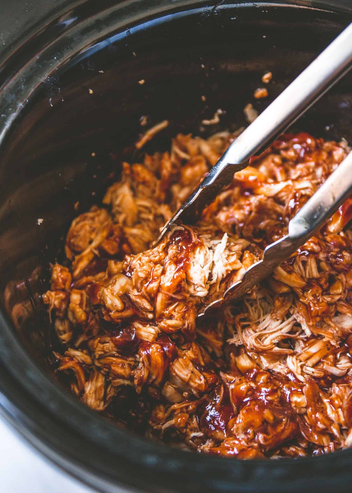 overhead image of tongs in BBQ Pulled Chicken in a slow cooker