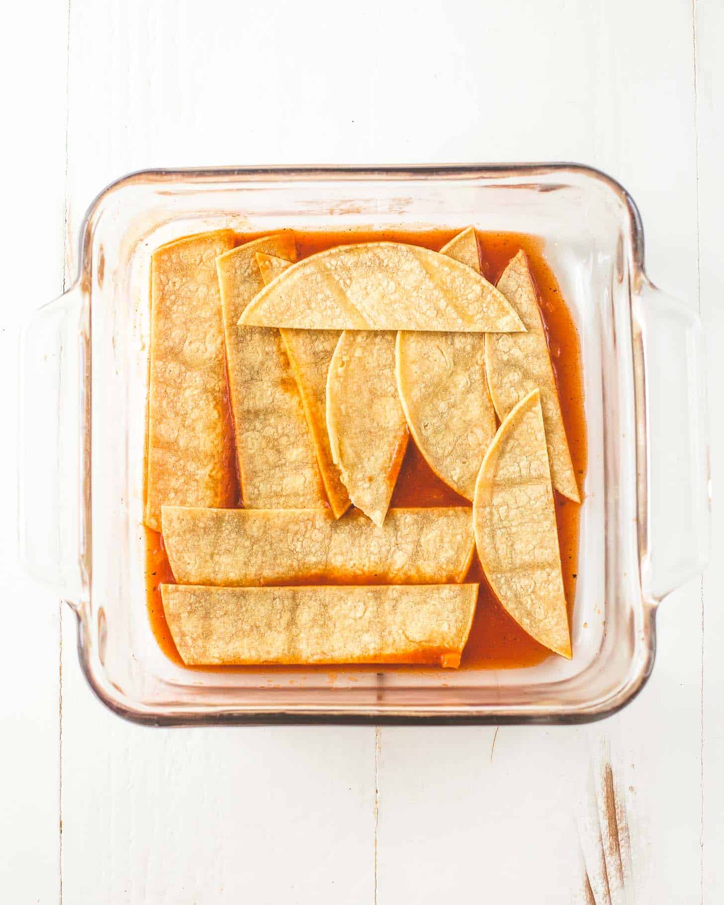 overhead image of tortillas and enchilada sauce in a square baking dish