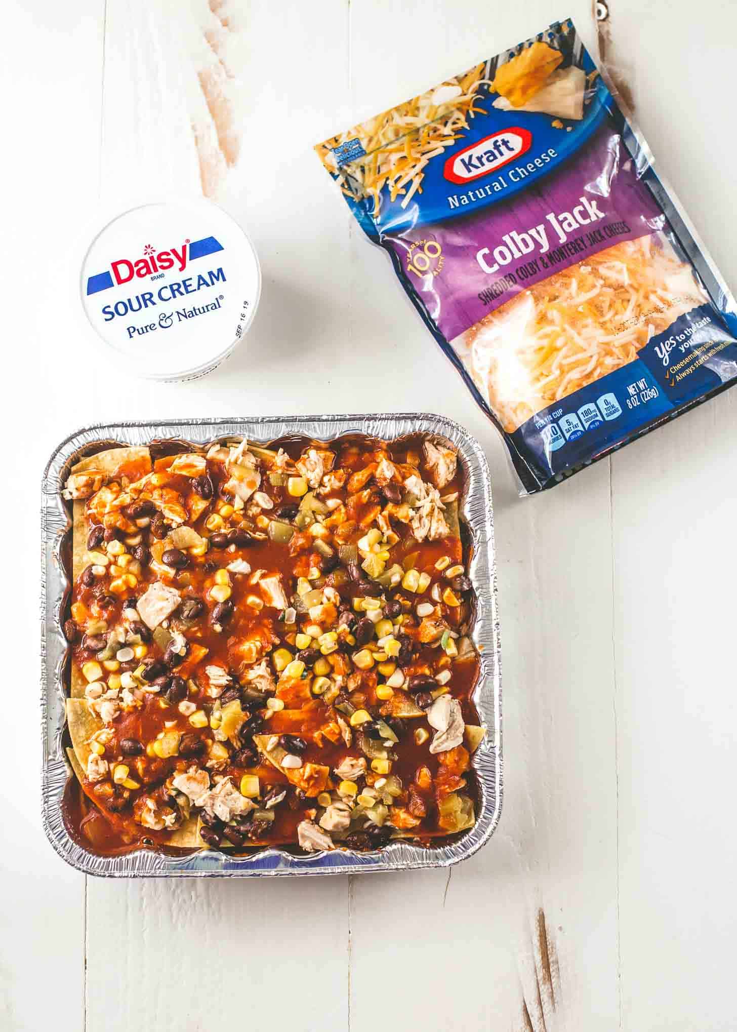 overhead image of Chicken Enchilada Casserole, sour cream and cheese on a white table