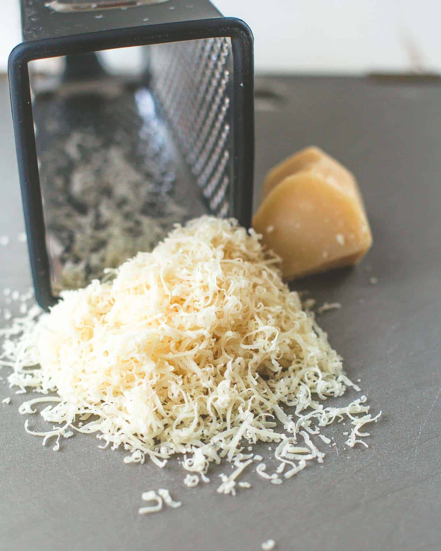 shredding parmesan cheese with a box grater on a grey cutting board