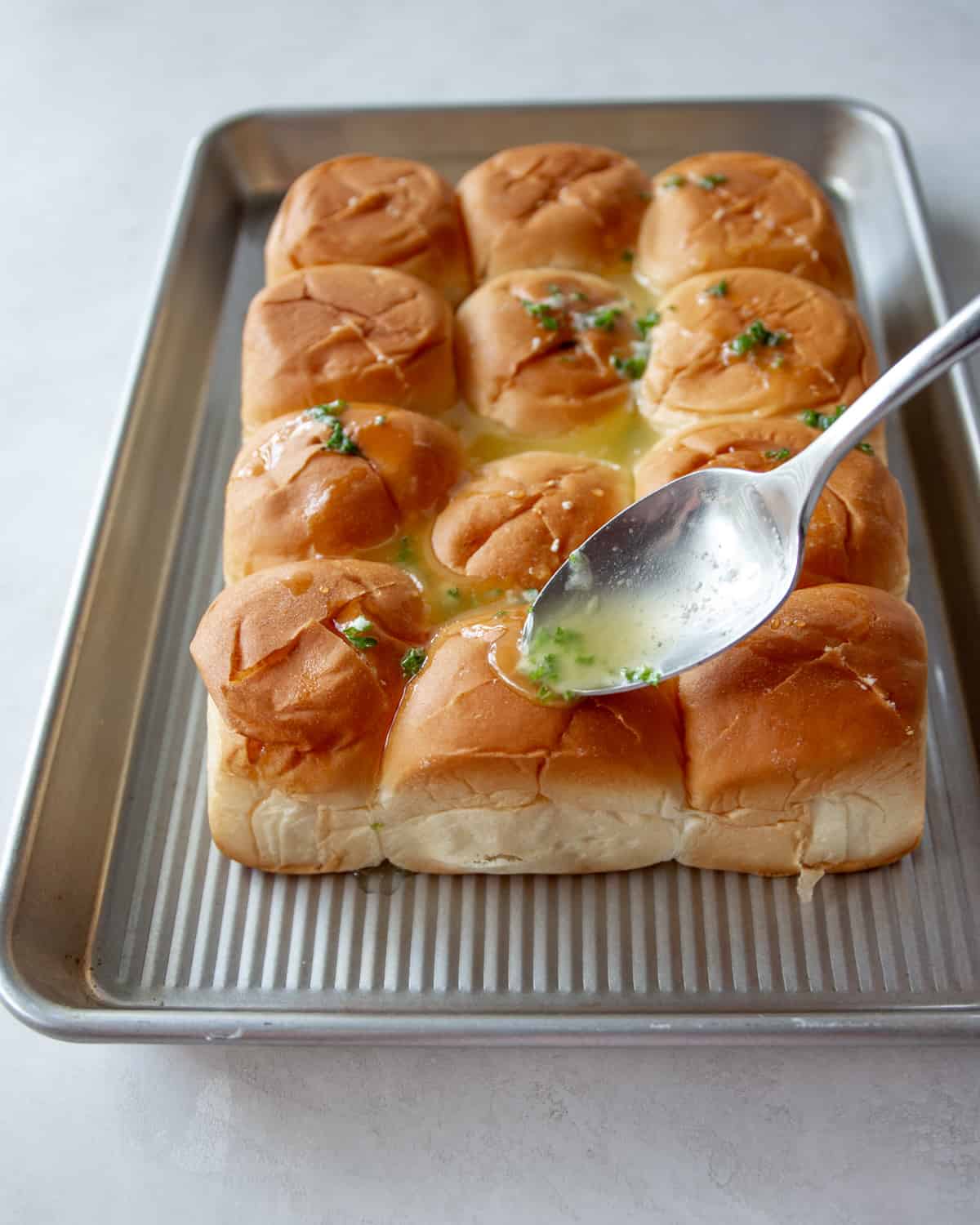 drizzling hawaiian rolls with garlic butter on a sheet pan