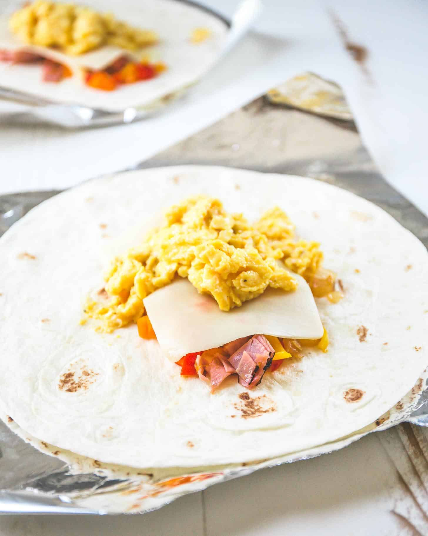 a tortilla topped with scrambled egg, ham and cheese