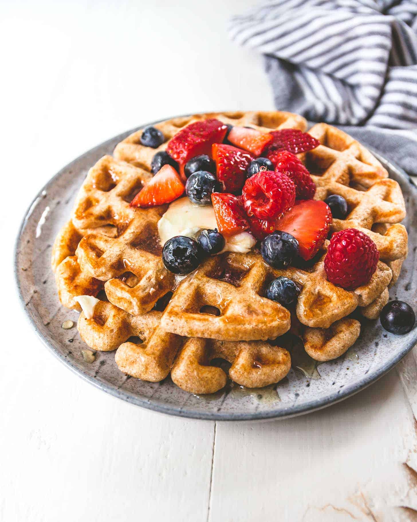 Waffles on a plate, topped with butter and berries