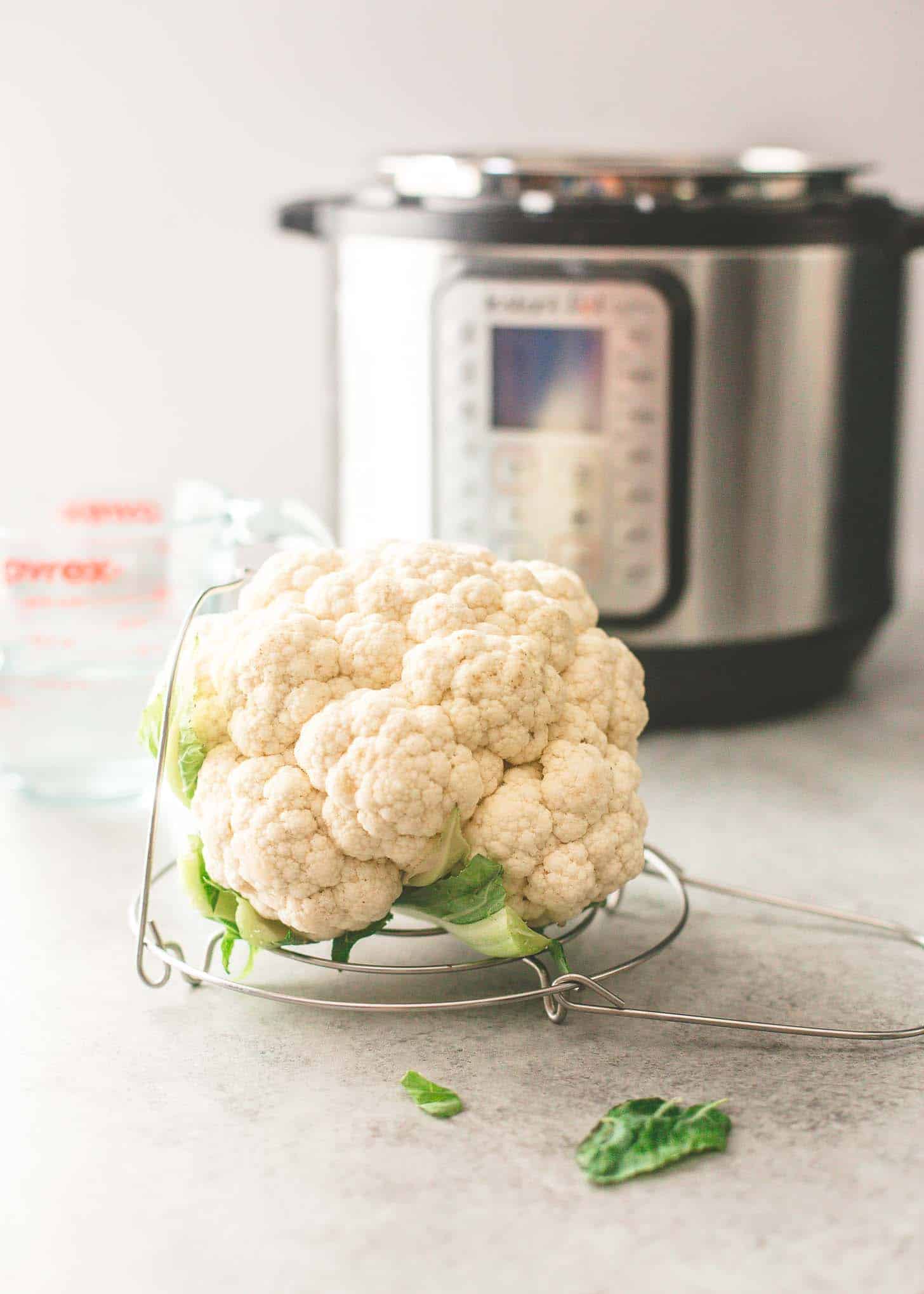 an uncooked head of cauliflower on a trivet for the instant pot