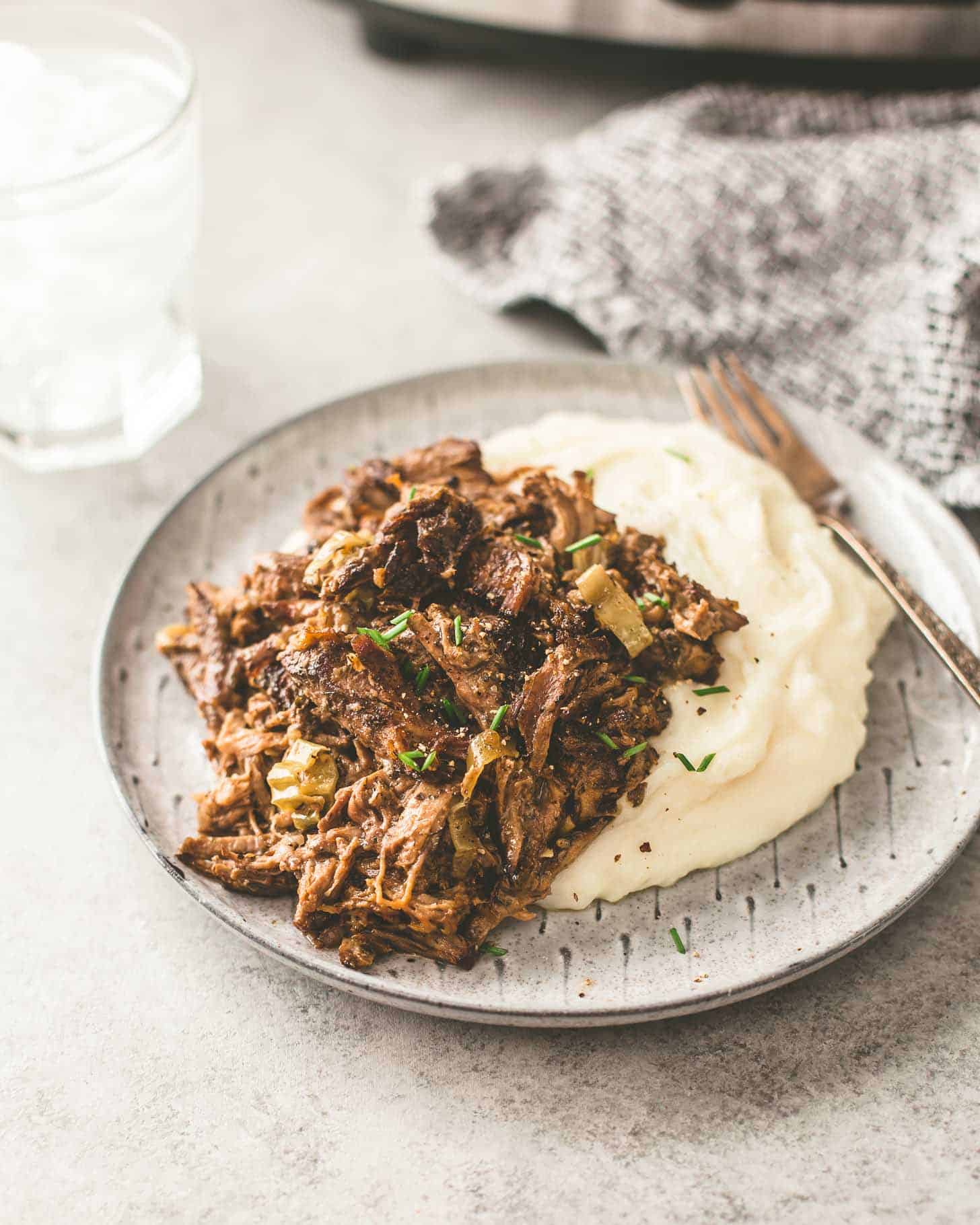 Slow Cooker Mississippi Roast over mashed potatoes on a grey plate