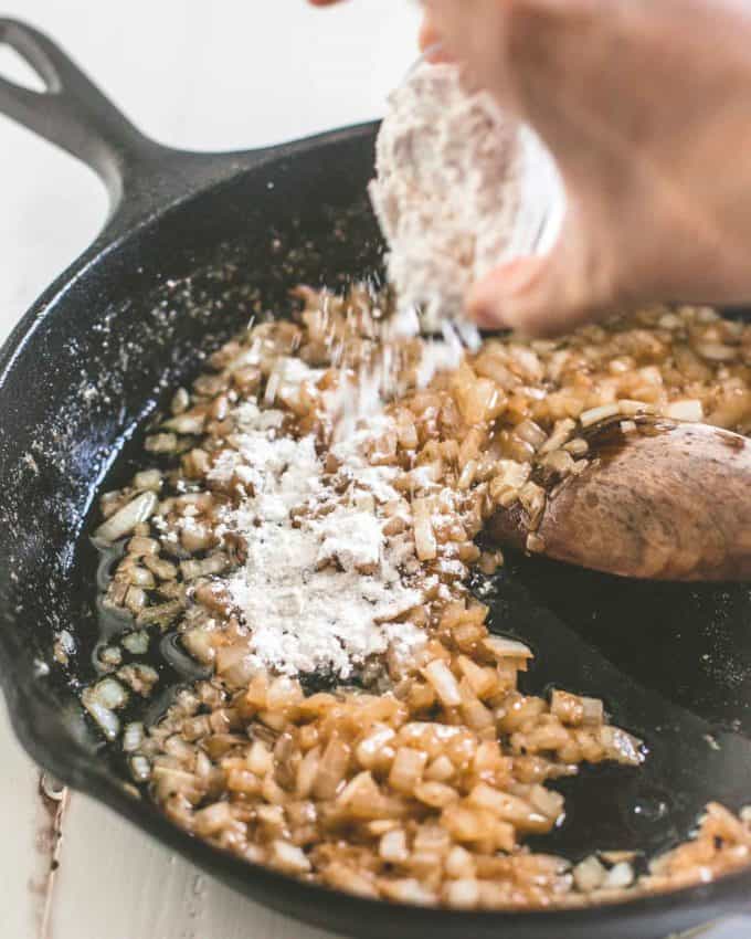 adding flour to onions in a skillet