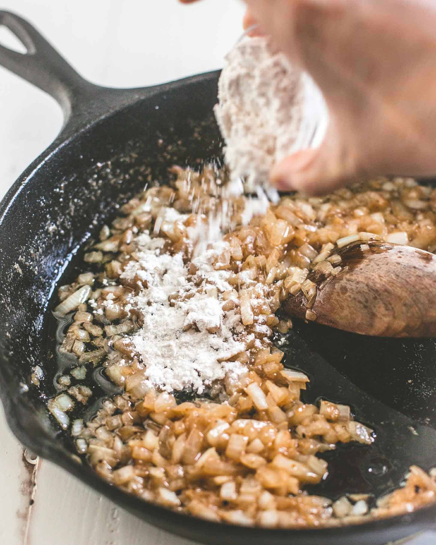 adding flour to onions in a cast iron skillet