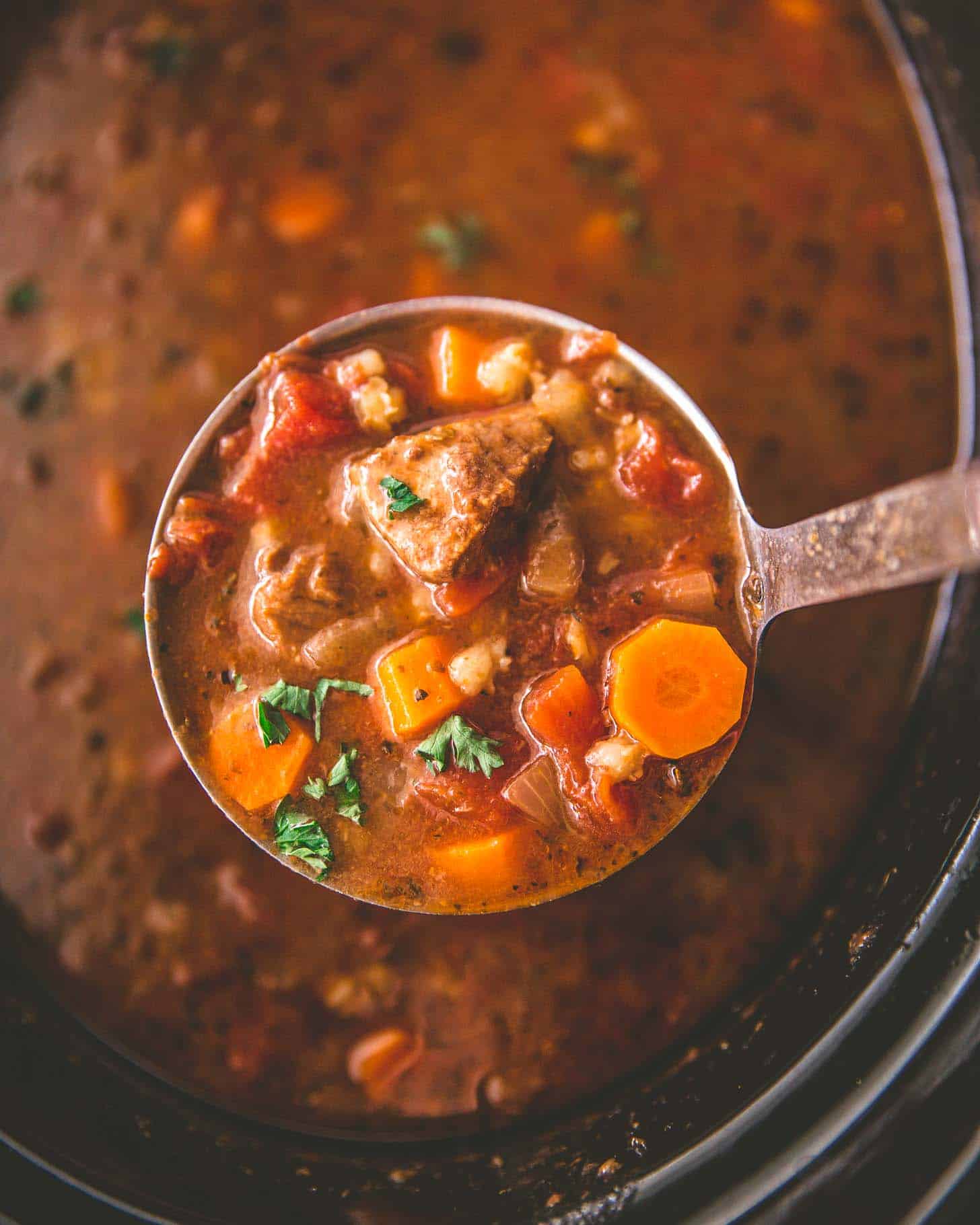 overhead image of a ladle of beef and barley soup