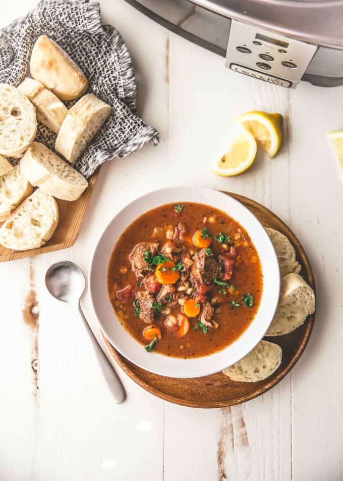 a bowl of beef and barley soup with slices of crusty bread