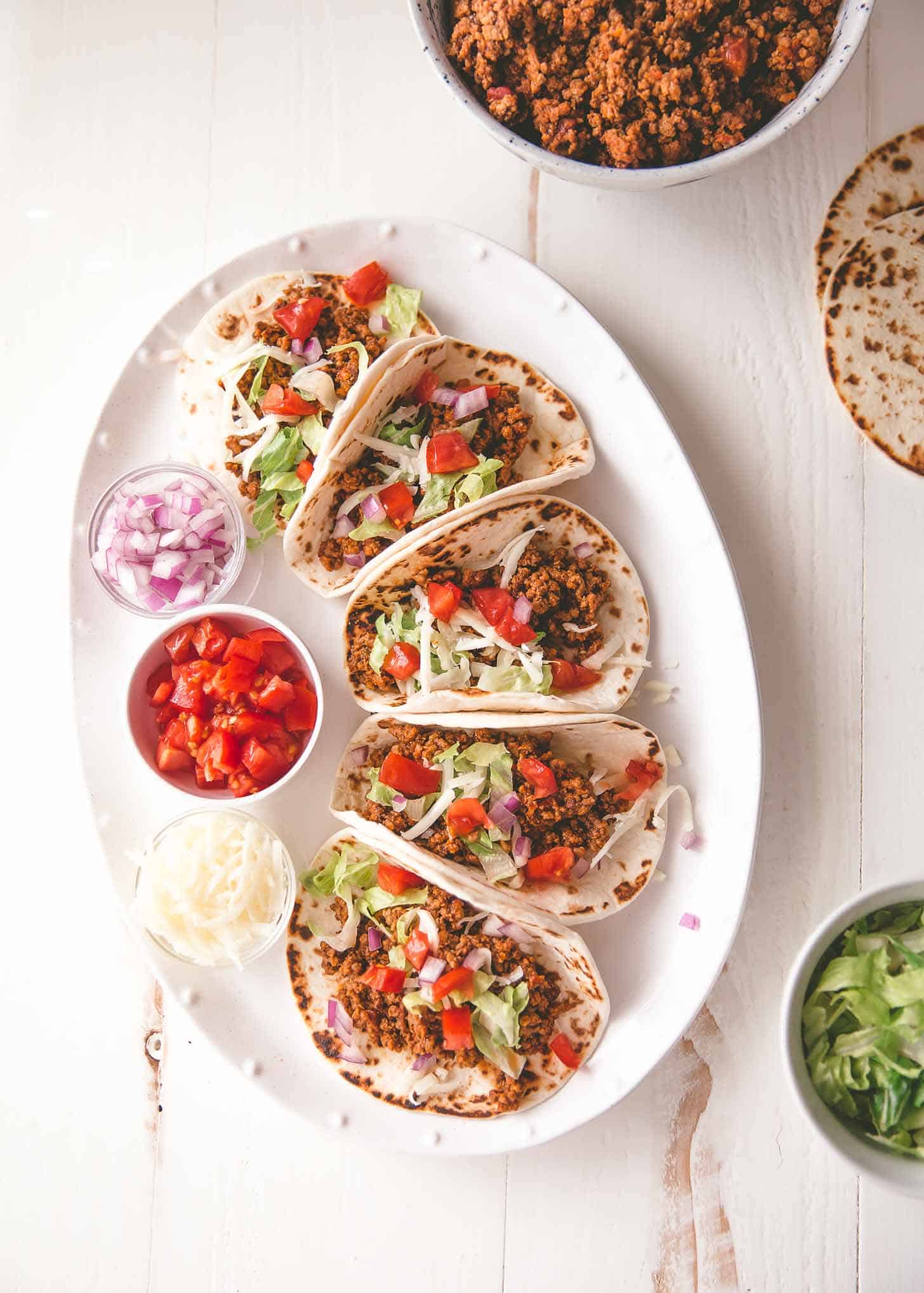 overhead image of tacos, tomatoes, onions and cheese on a white tray