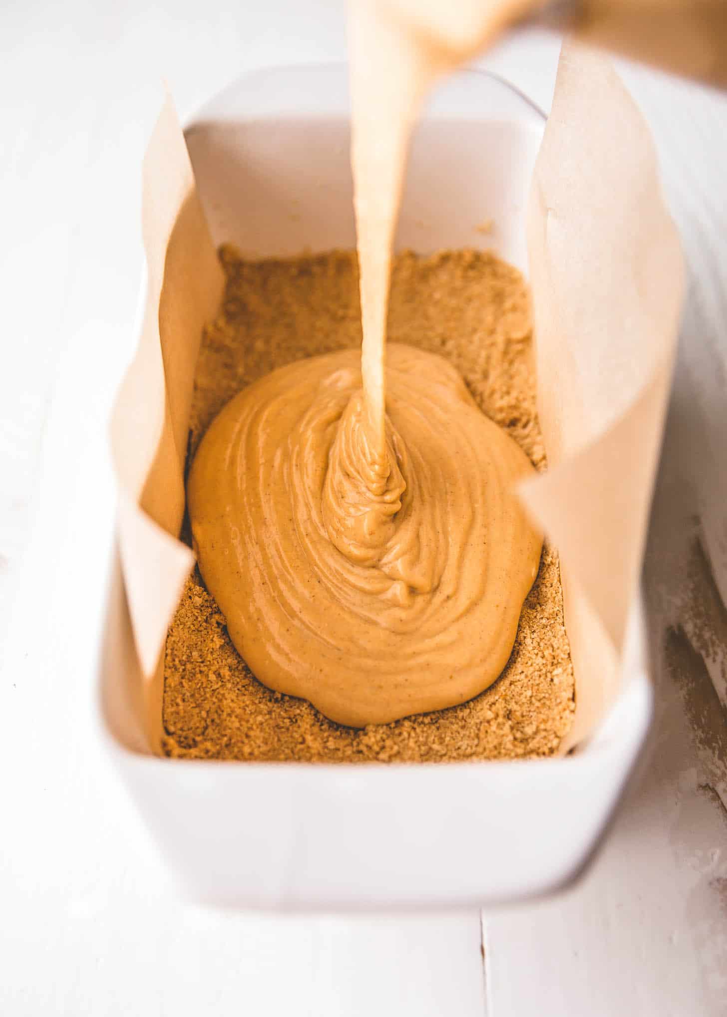 pouring cheesecake mix over crust in loaf pan