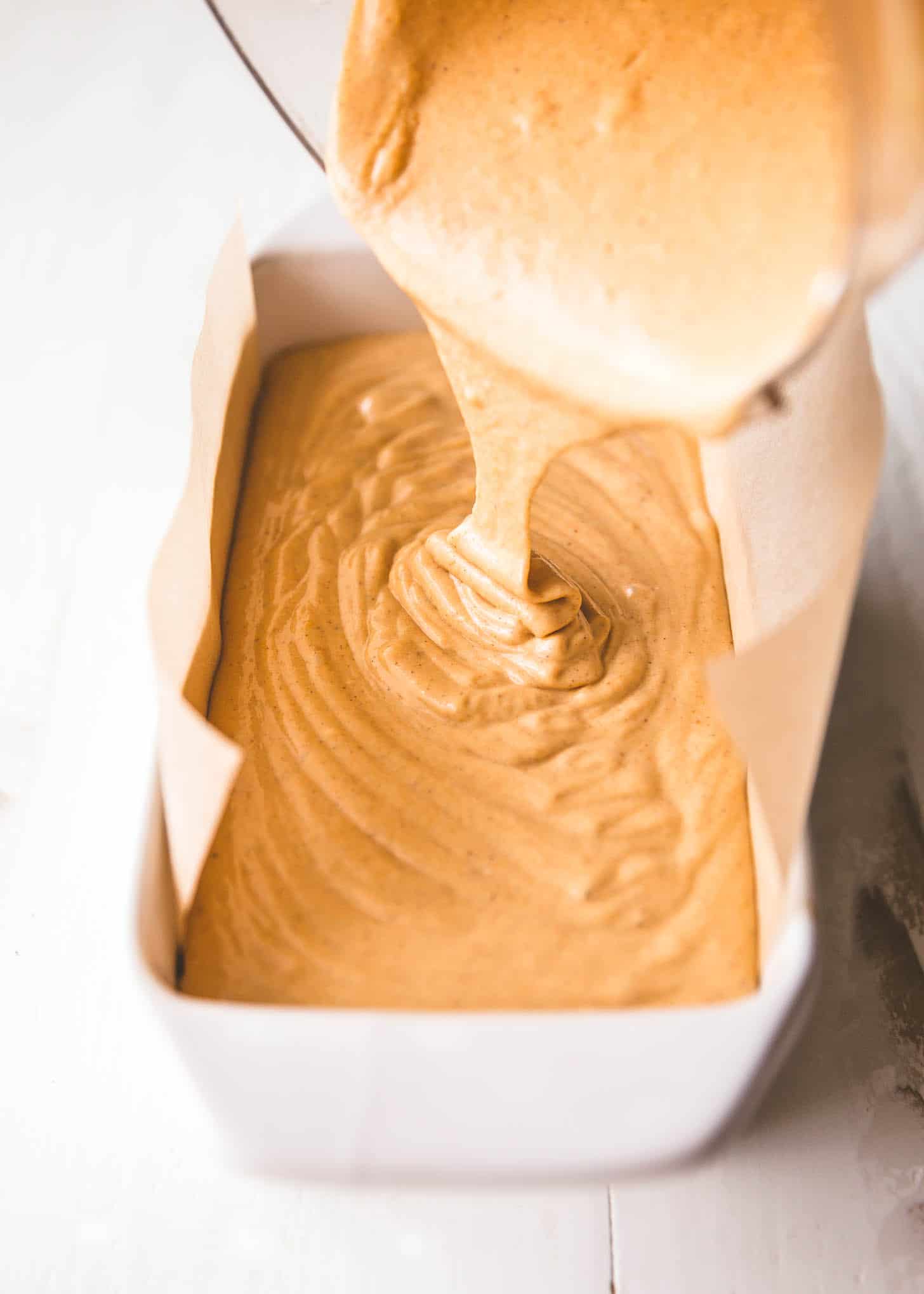 pouring cheesecake mixture into parchment lined loaf pan