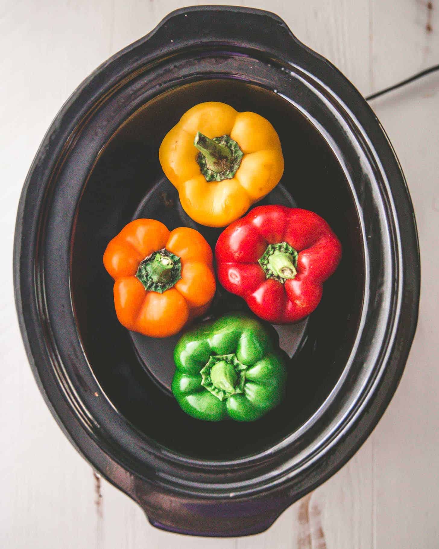 overhead image of red, yellow, and orange bell peppers in a slow cooker