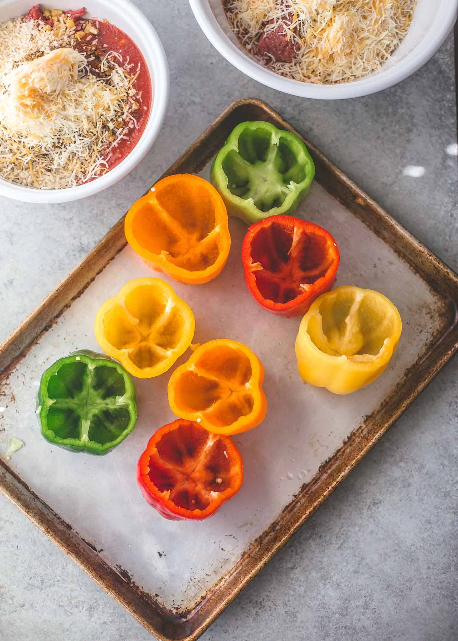 overhead image of raw bell peppers with the tops cut off, sitting on a sheet pan