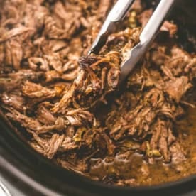 the bowl of a slow cooker with shredded pork mississippi roast