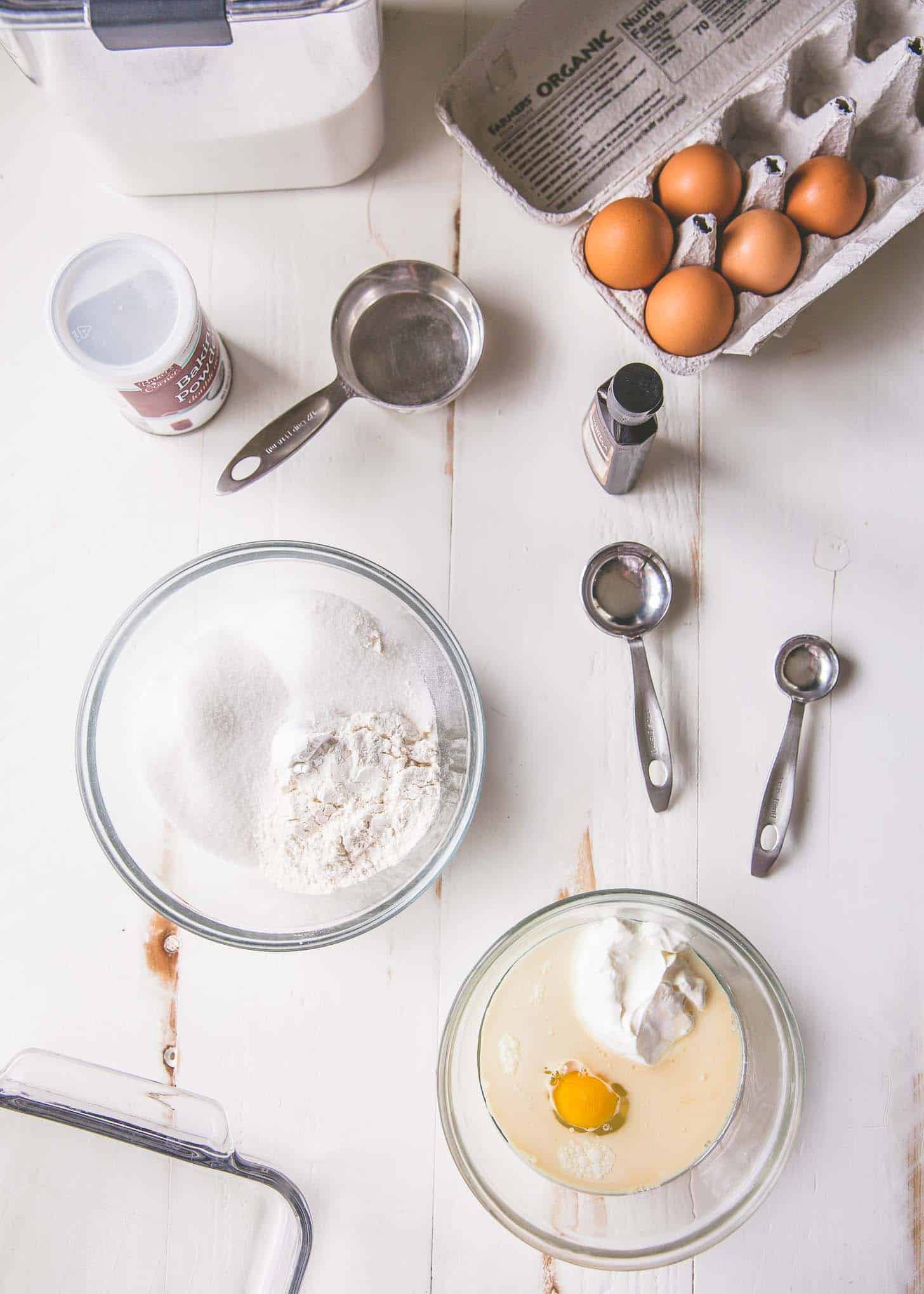 eggs, sugar, flour, vanilla, baking powder and measuring spoons on a white table