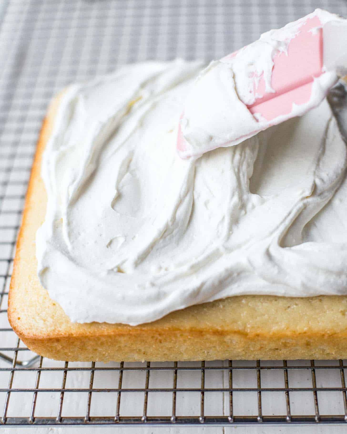 spreading vanilla frosting on a cake with a spatula