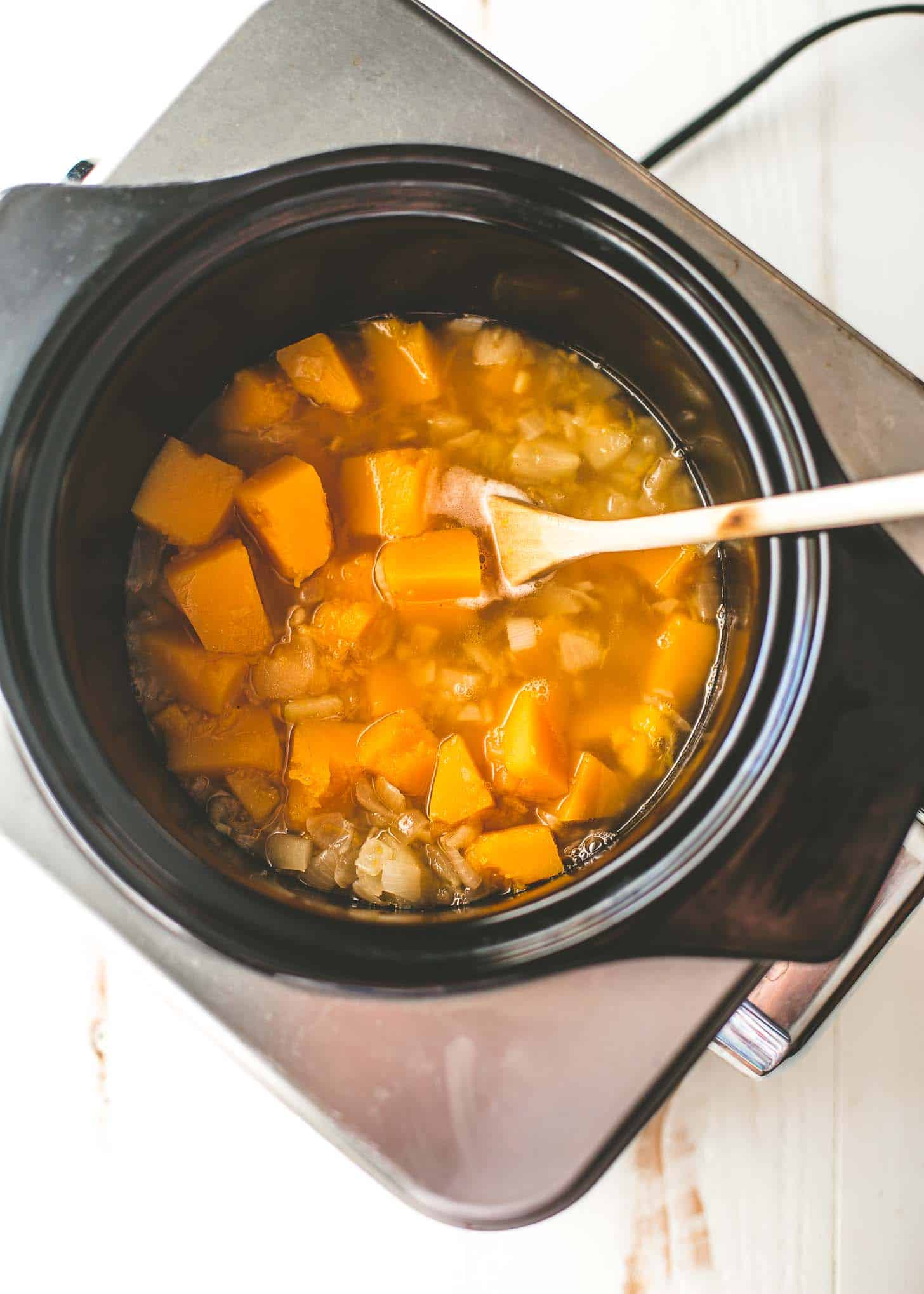 overhead image of a wooden spoon stirring butternut squash in a slow cooker