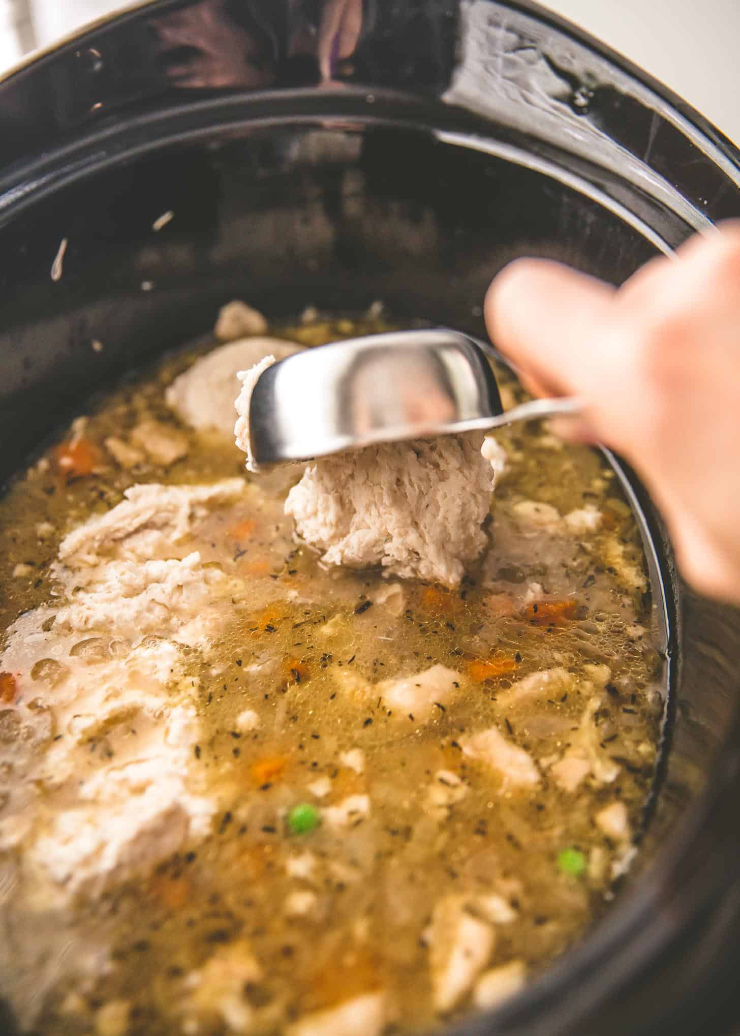 adding biscuits to chicken and broth in a slow cooker