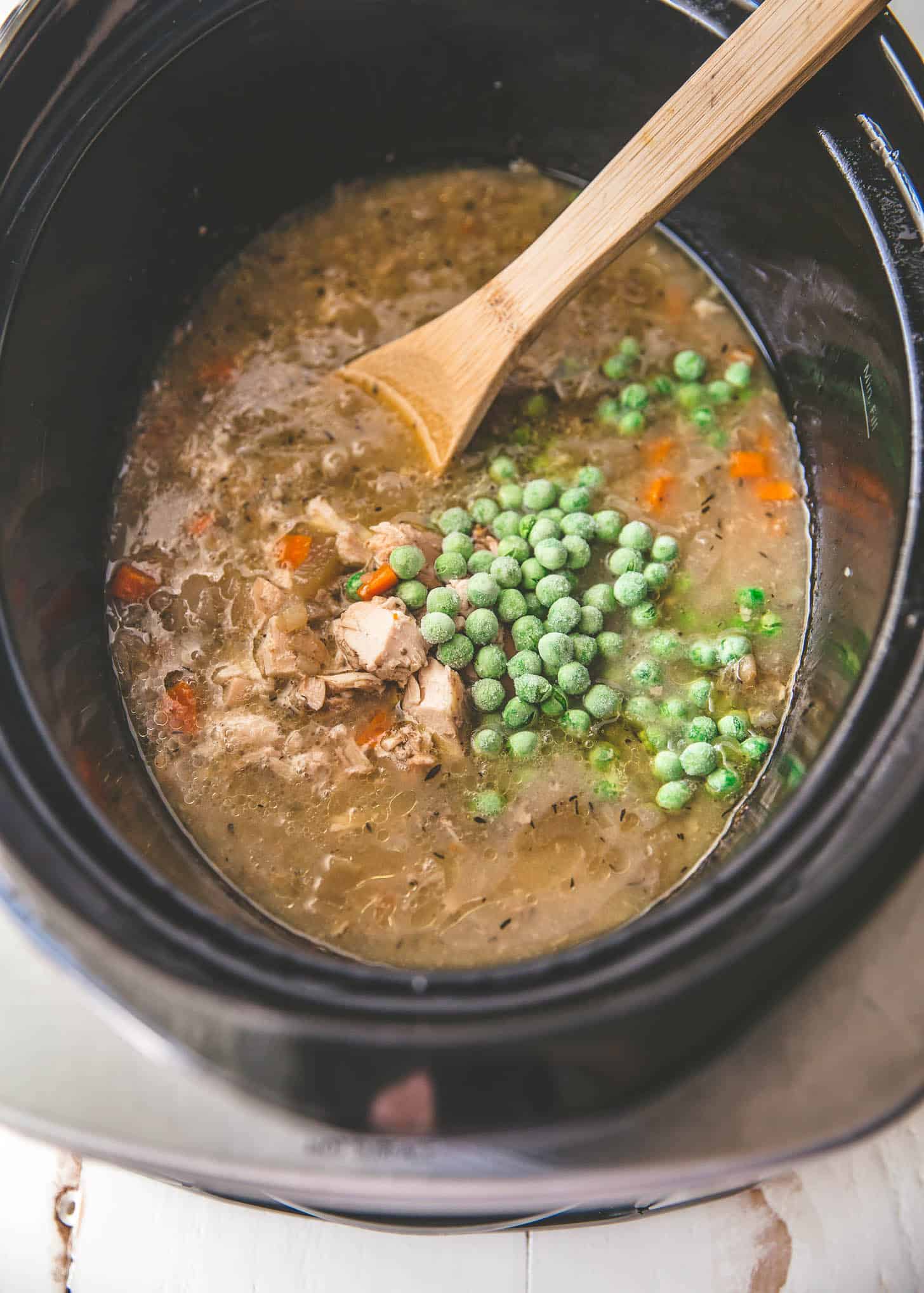 overhead image of stirring vegetables into chicken broth in the slow cooker