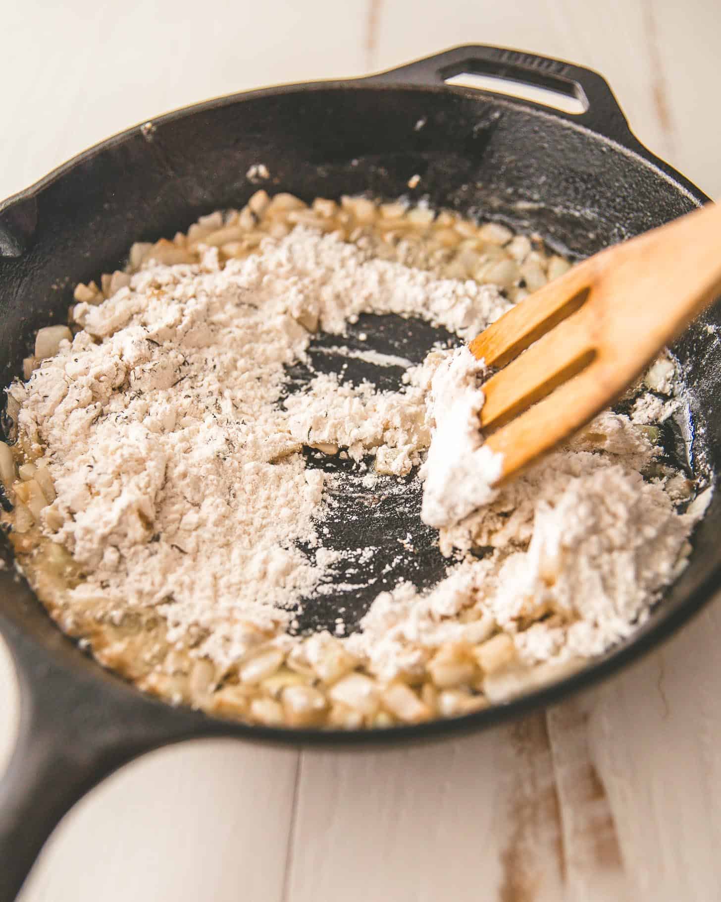 adding flour to sautéed onions in a cast iron skillet