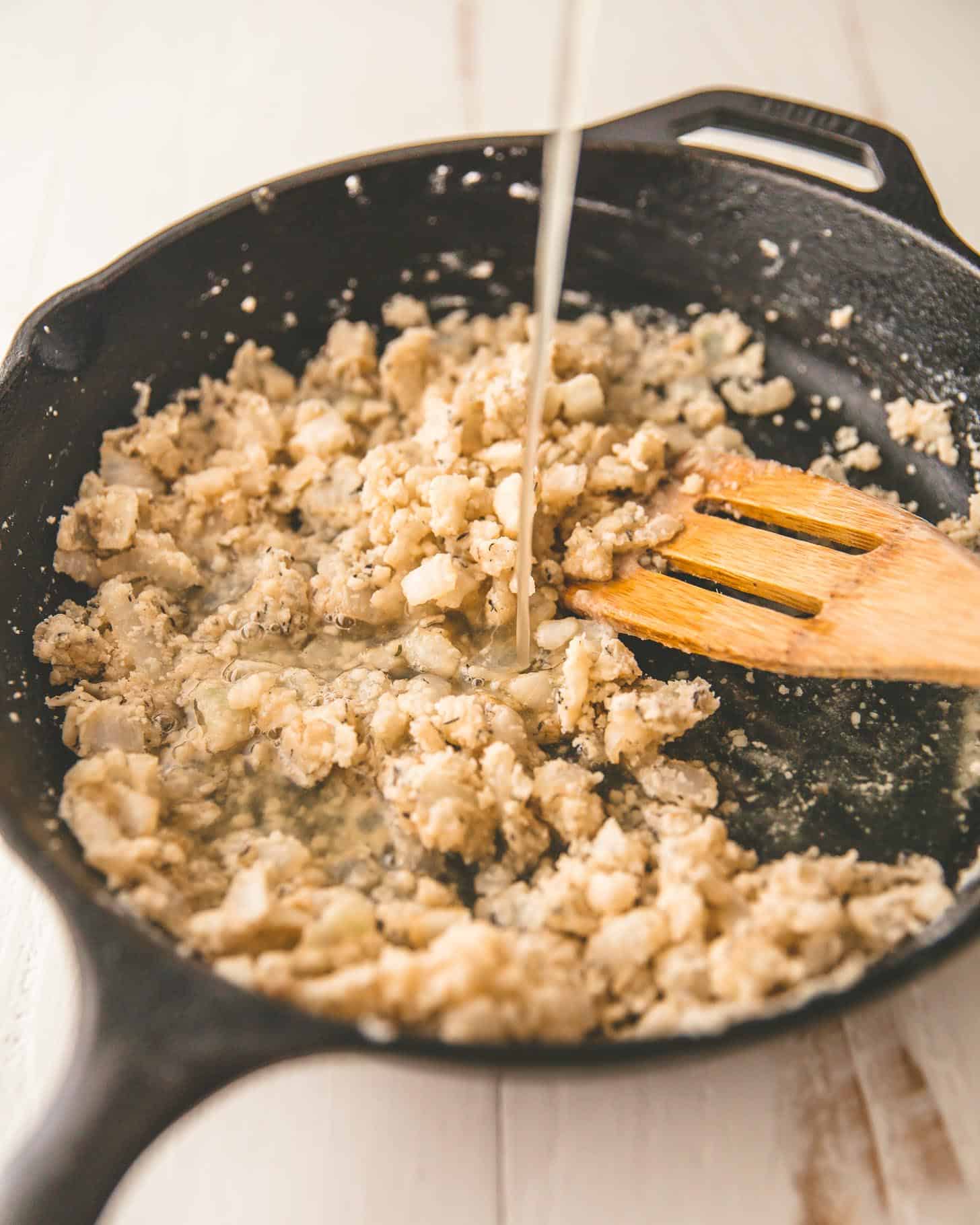 adding broth to onions in a cast iron skillet