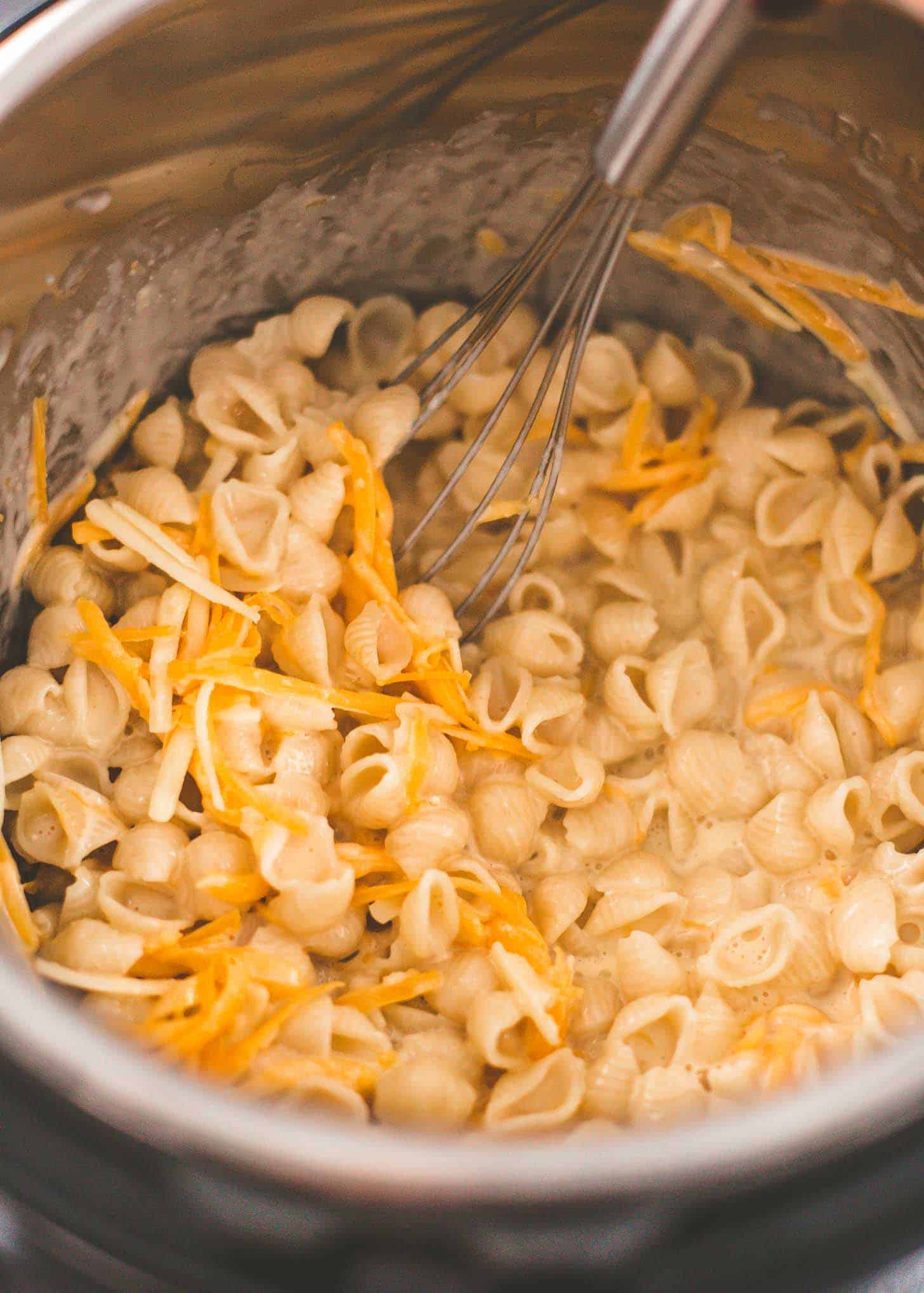 stirring cheese into pasta in the bowl of a pressure cooker