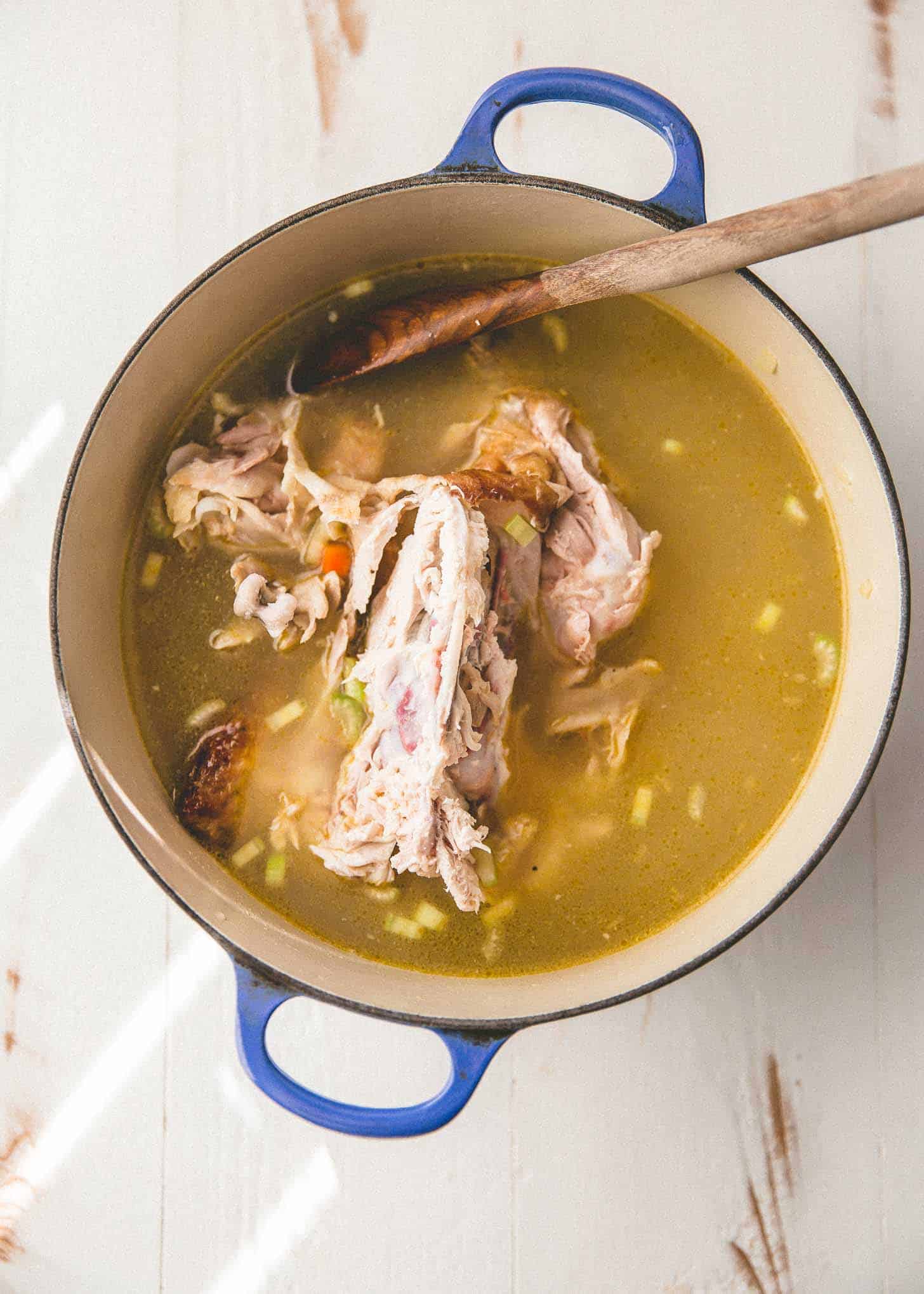 overhead image of cooking a chicken in broth in a blue dutch oven