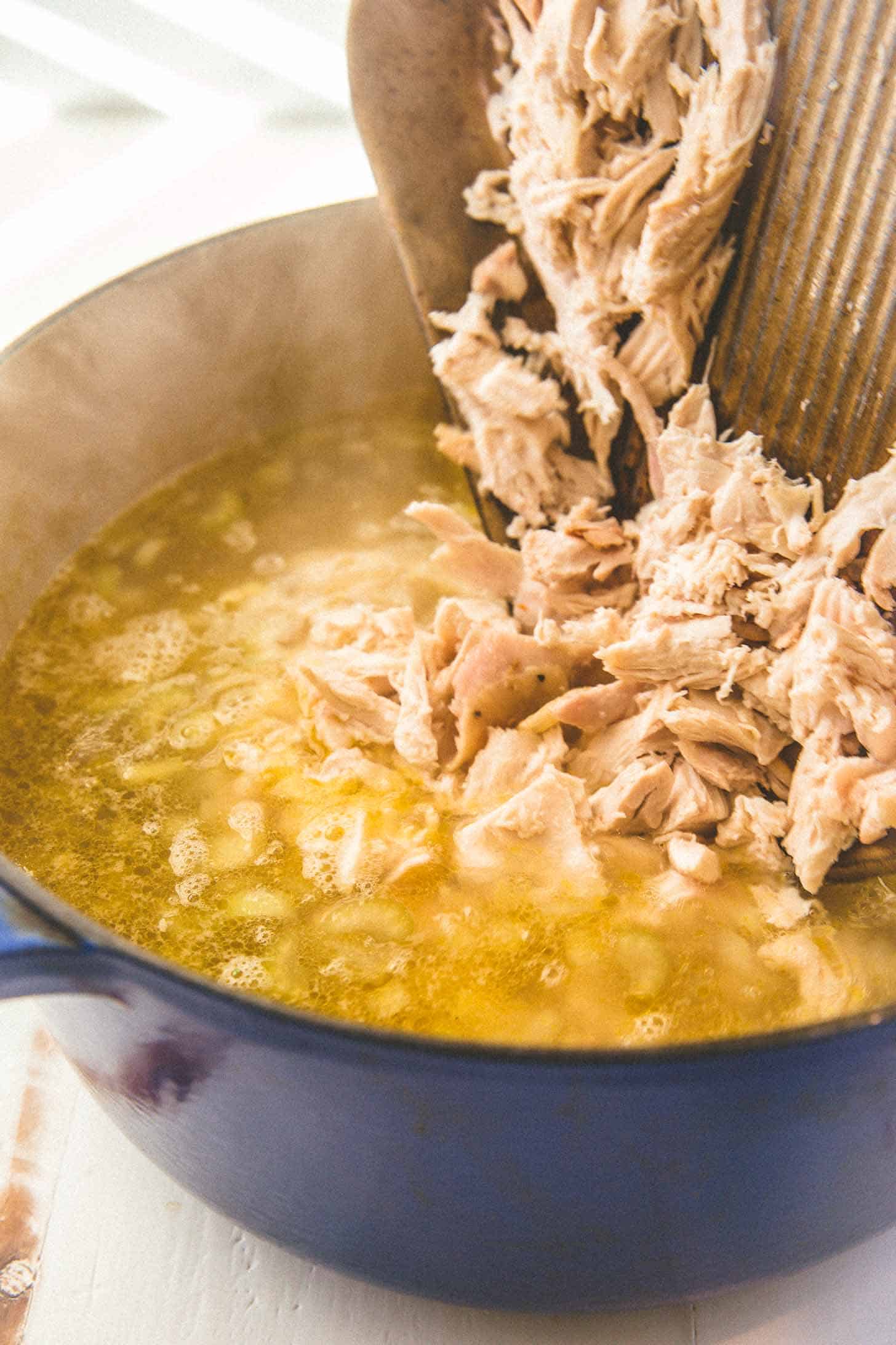 adding chopped chicken to soup in a blue dutch oven