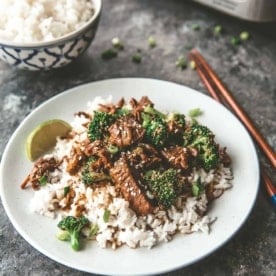 beef and broccoli over rice on a white plate