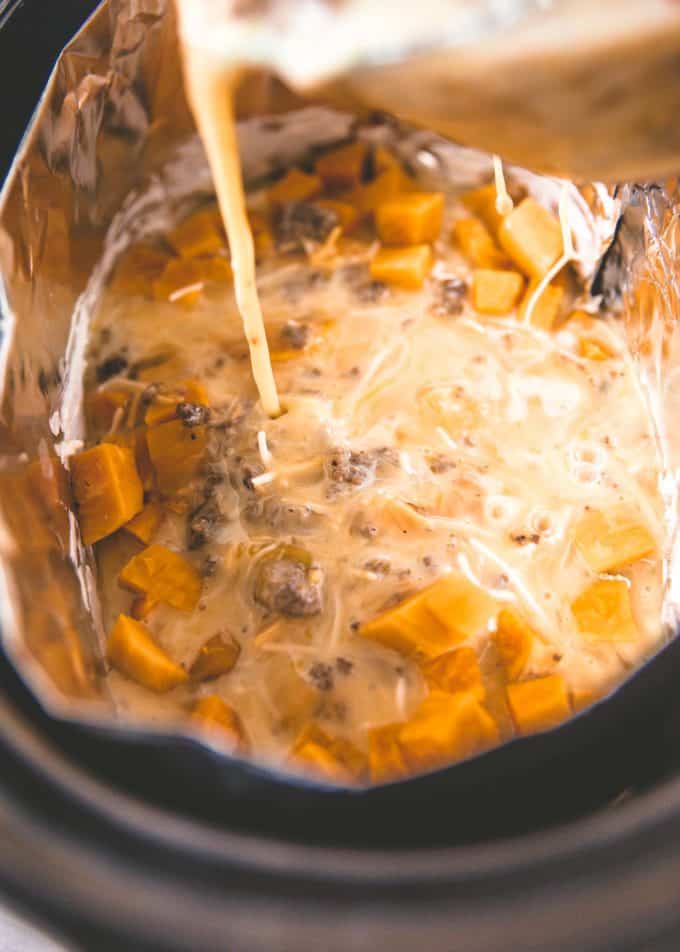 adding egg mixture to sweet potatoes and sausage in the slow cooker