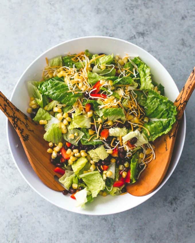 salad in a white bowl with two wooden spoons