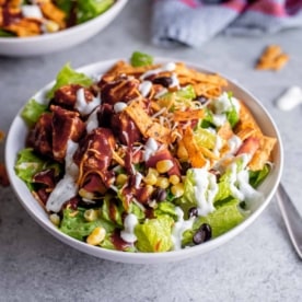 square image of romaine lettuce salad topped with corn, black beans, tortilla strips, and bbq chicken