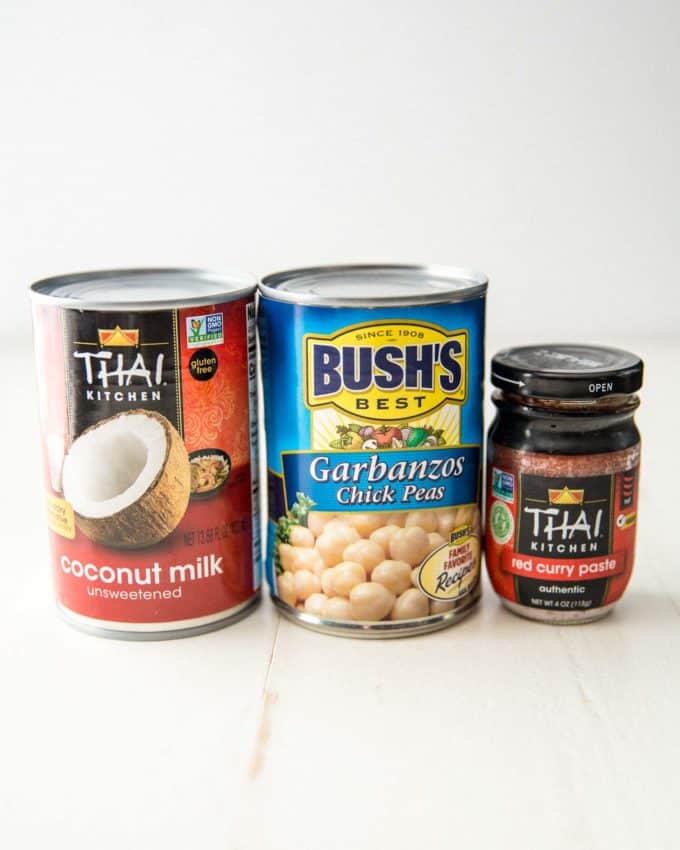 cans of coconut milk, garbanzo beans, and a jar of red curry paste on a white table