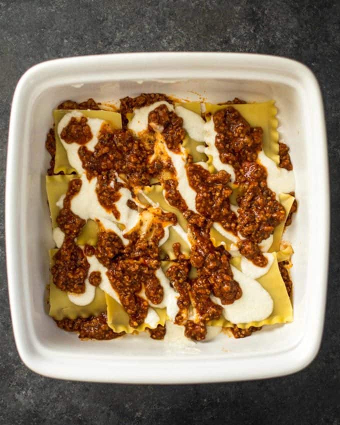 uncooked lasagna bolognese in a white baking dish