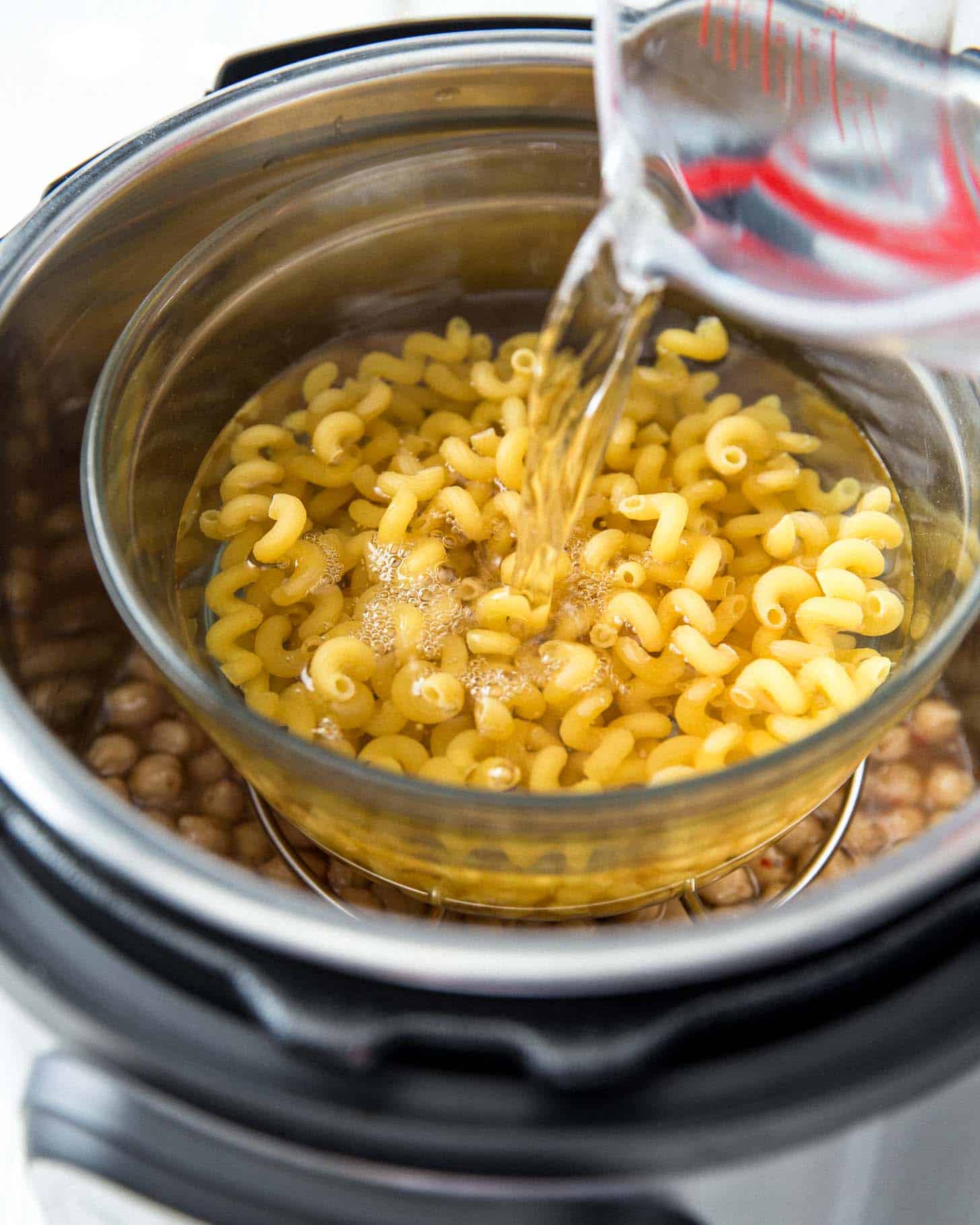 adding water to a bowl of uncooked pasta in an Instant Pot