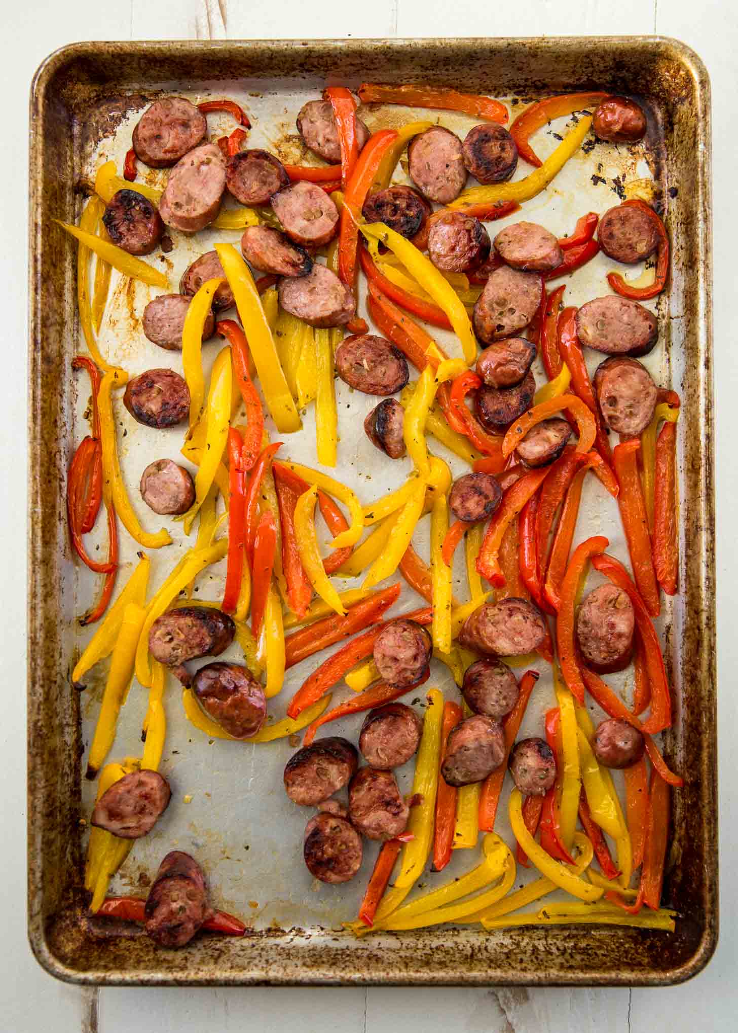 overhead image of cooked sausage and red and yellow peppers on a sheet pan