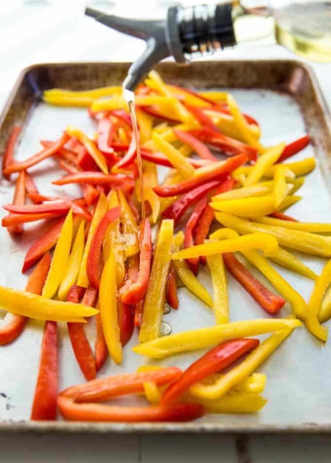 drizzling olive oil onto cut yellow and red bell peppers on a sheet pan