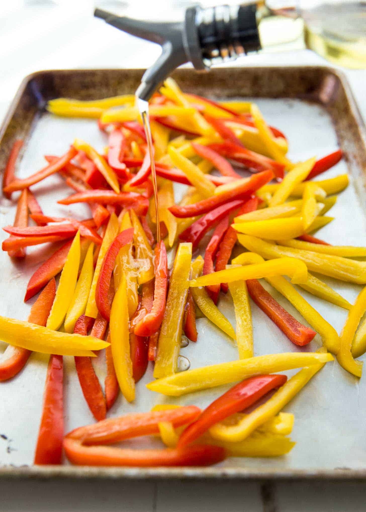 drizzling olive oil onto cut yellow and red bell peppers on a sheet pan