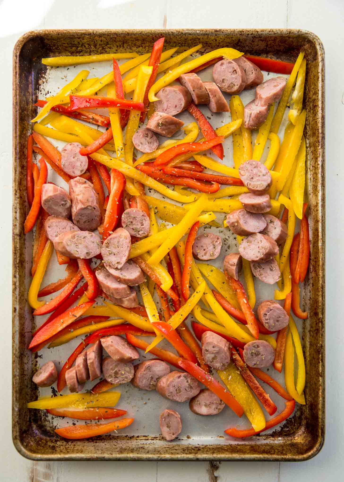 overhead image of uncooked sausage and peppers on a sheet pan