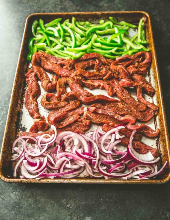 uncooked steak, peppers and onions on a sheet pan